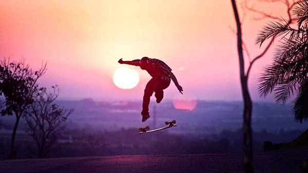 夕日をバックにスケボーのトリックを決める男性