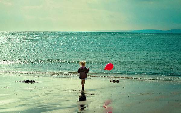海辺で風船を持って遊ぶ少女を撮影したフリー写真画像