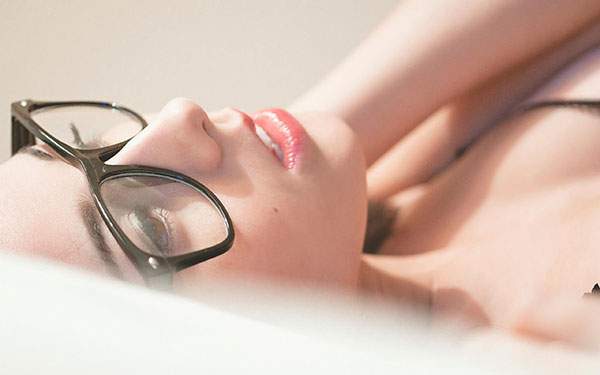 黒縁メガネをかけてベットに寝そべった女性の綺麗な写真壁紙