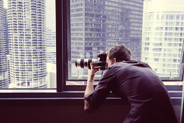 ビルの窓から撮影するカメラマンの写真